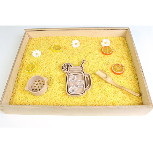 kids-kabinet-vulvorm-pla-limonadeglas (2) Houten speelbak gevuld met gele speelrijst, met bloemen en citroenschijven. Zeefje en schepje met lange steel, vultray of vulvorm limonadeglas van PLA (geperst tarwestro)